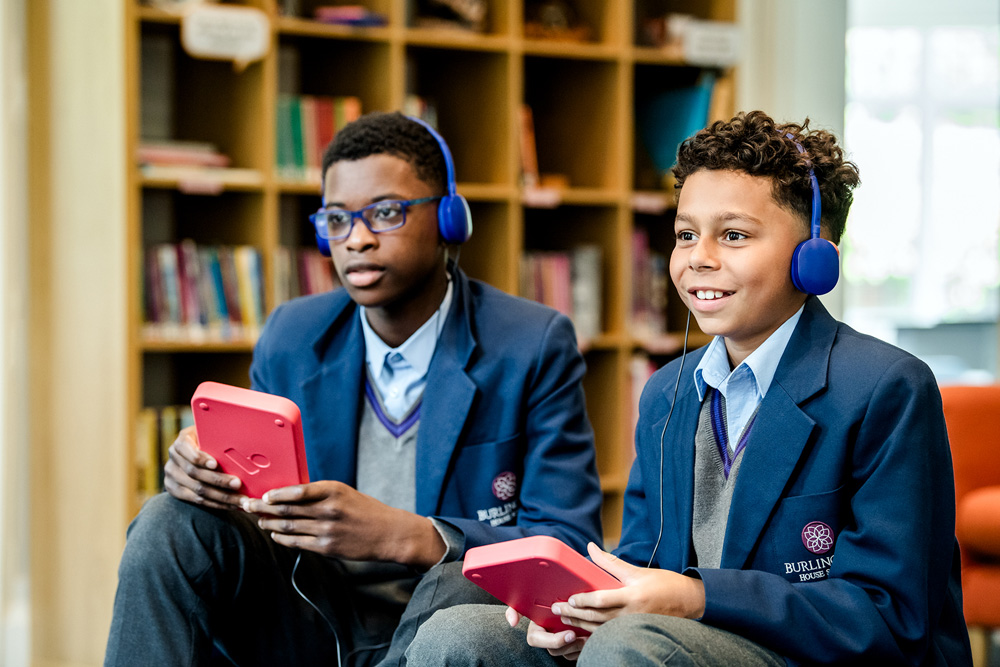 Two students in school library setting with headphones playing interactive game