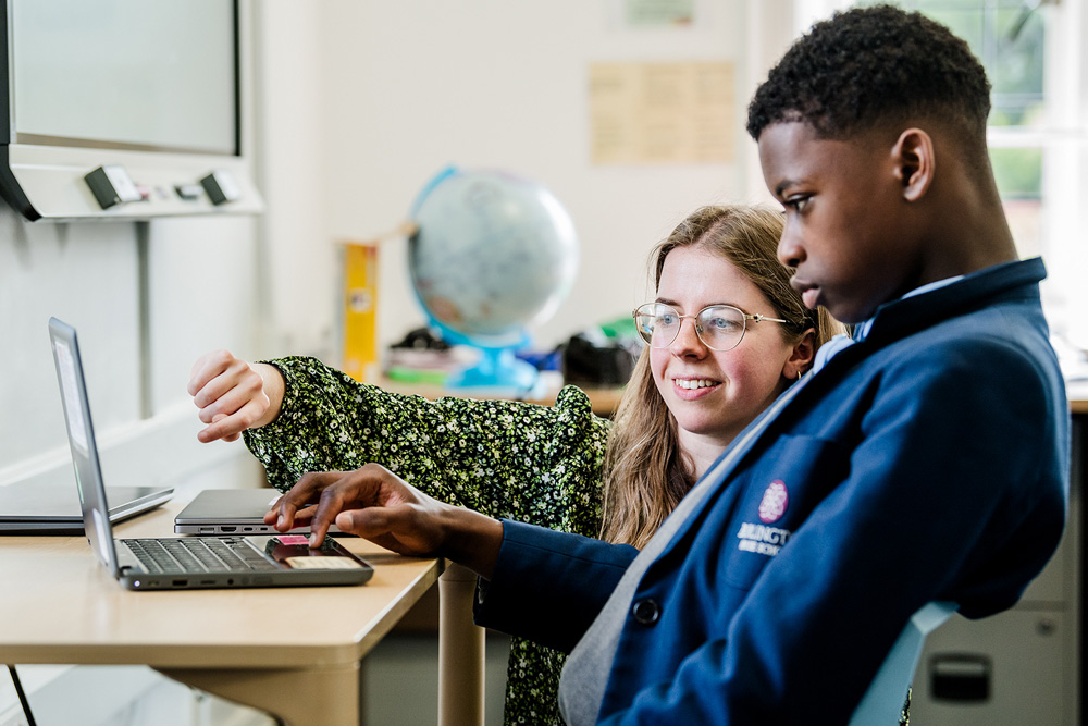 Young Black Male student looking at laptop in conversation with teacher in school classroom